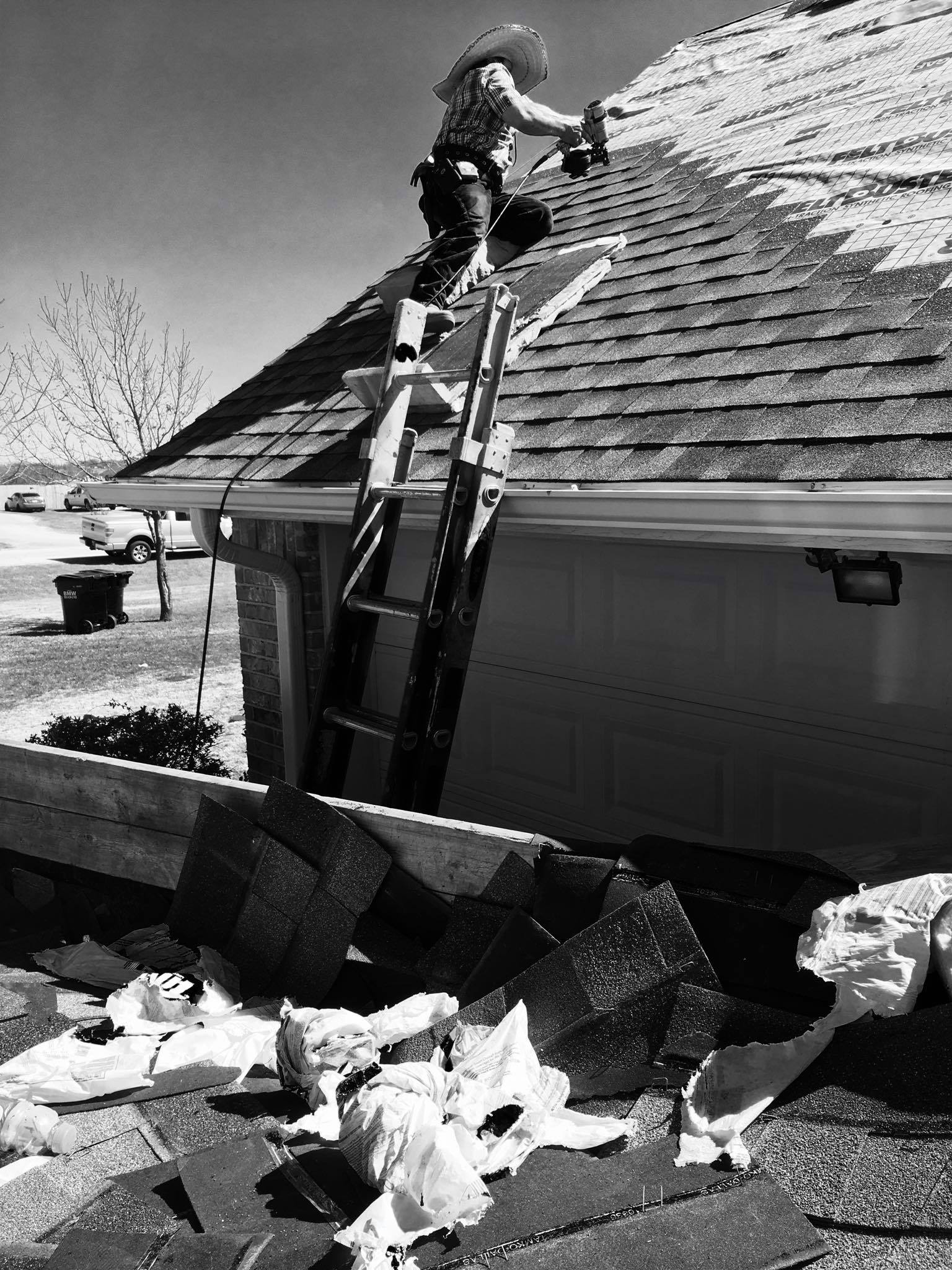 Crew member on ladder during roof installation installing shingles with a nailgun